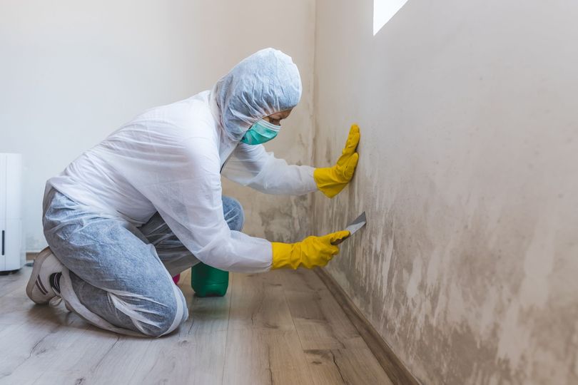 A man in a protective suit and mask is cleaning a wall.