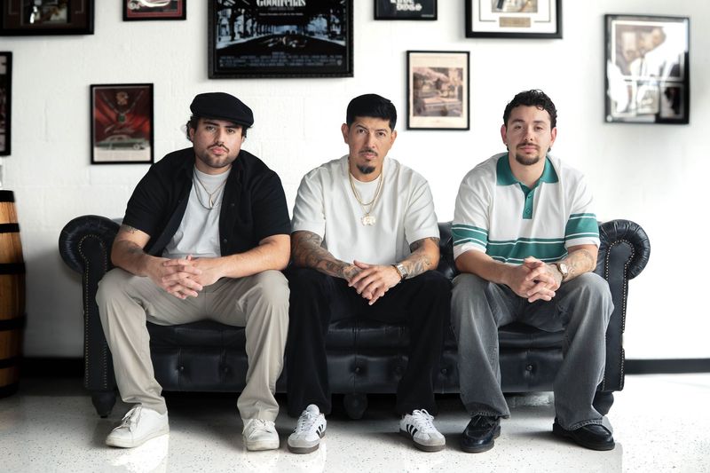 Three Goodfellas barbers seated on a black leather sofa inside the Schererville barbershop