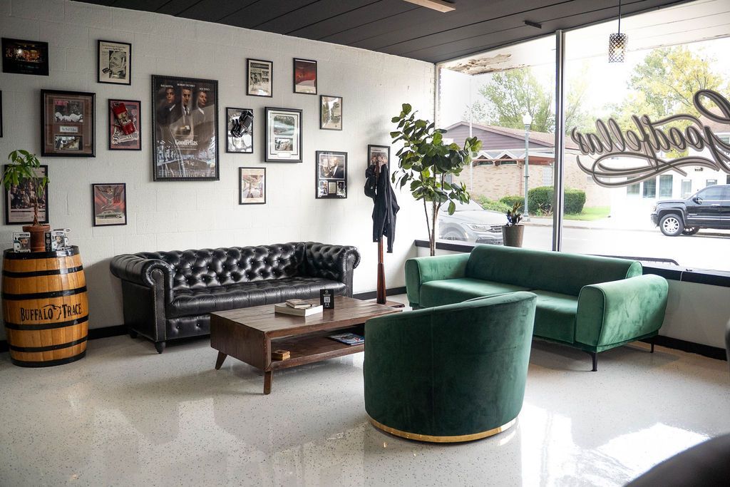 Waiting area with leather and green velvet sofas beside the Goodfellas front window at Goodfellas Barbershop in Schererville