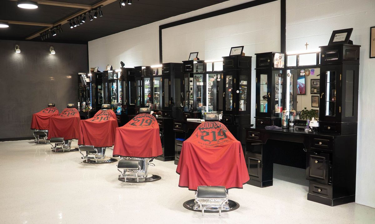 Row of barber chairs with red capes facing black mirror stations inside Goodfellas Barbershop in Schererville