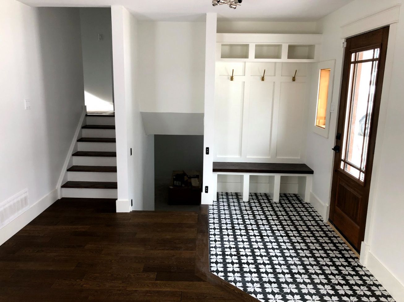 Entryway with a dark wood floor and staircase, a patterned tile floor, and a built-in coat rack and bench.