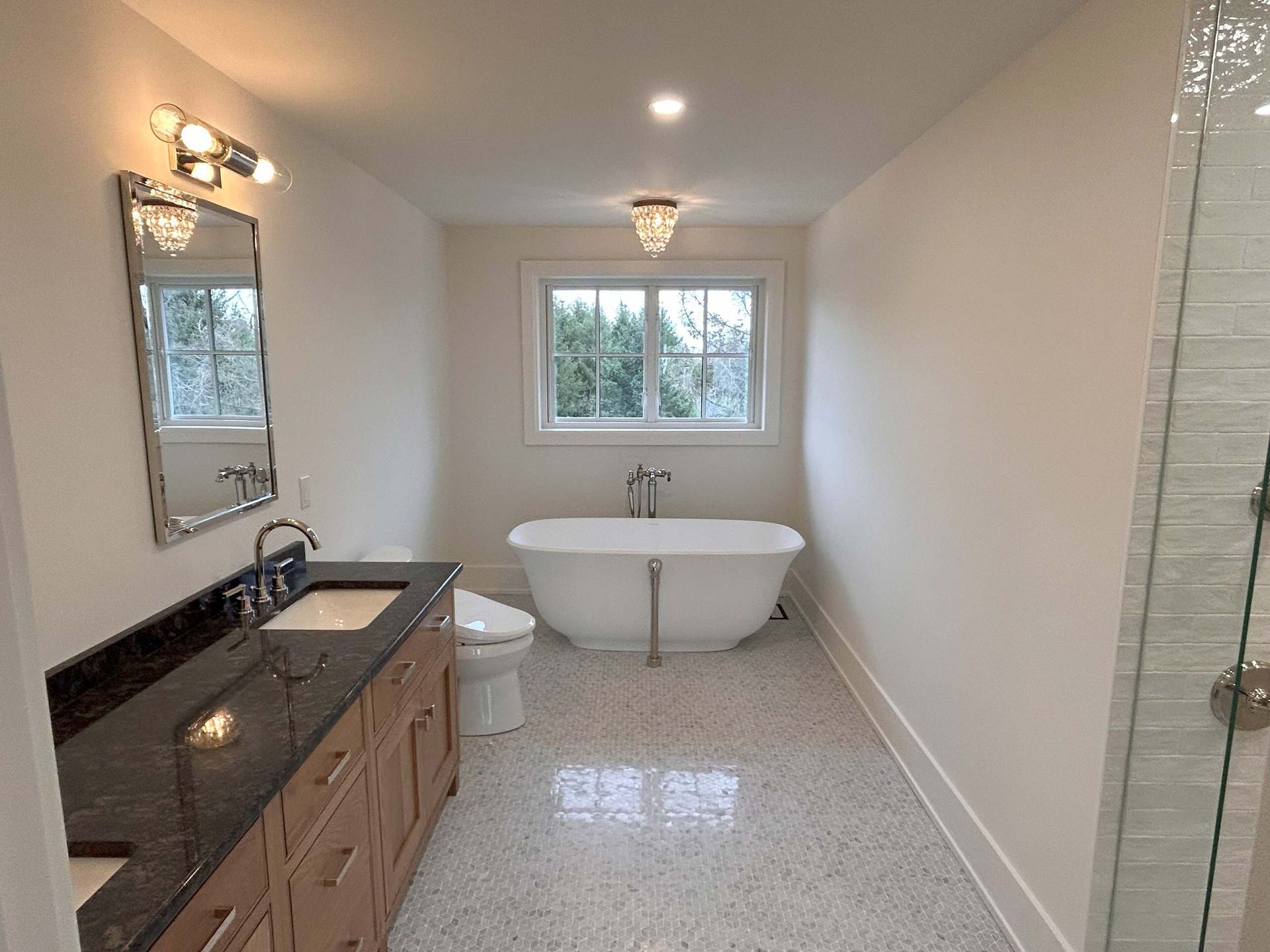 Bathroom with a white tub, vanity with dark counter, and neutral colored walls and flooring.