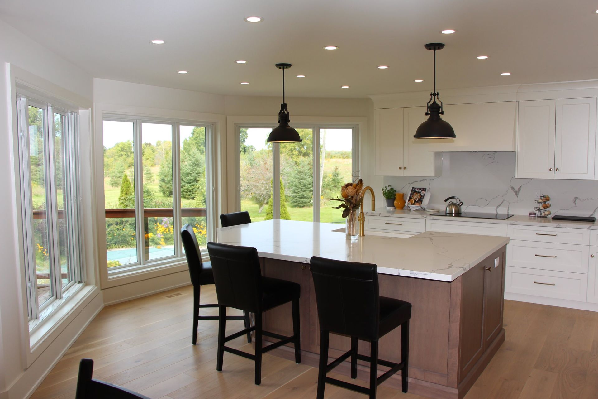 Kitchen with island, windows overlooking green landscape, and black bar stools.