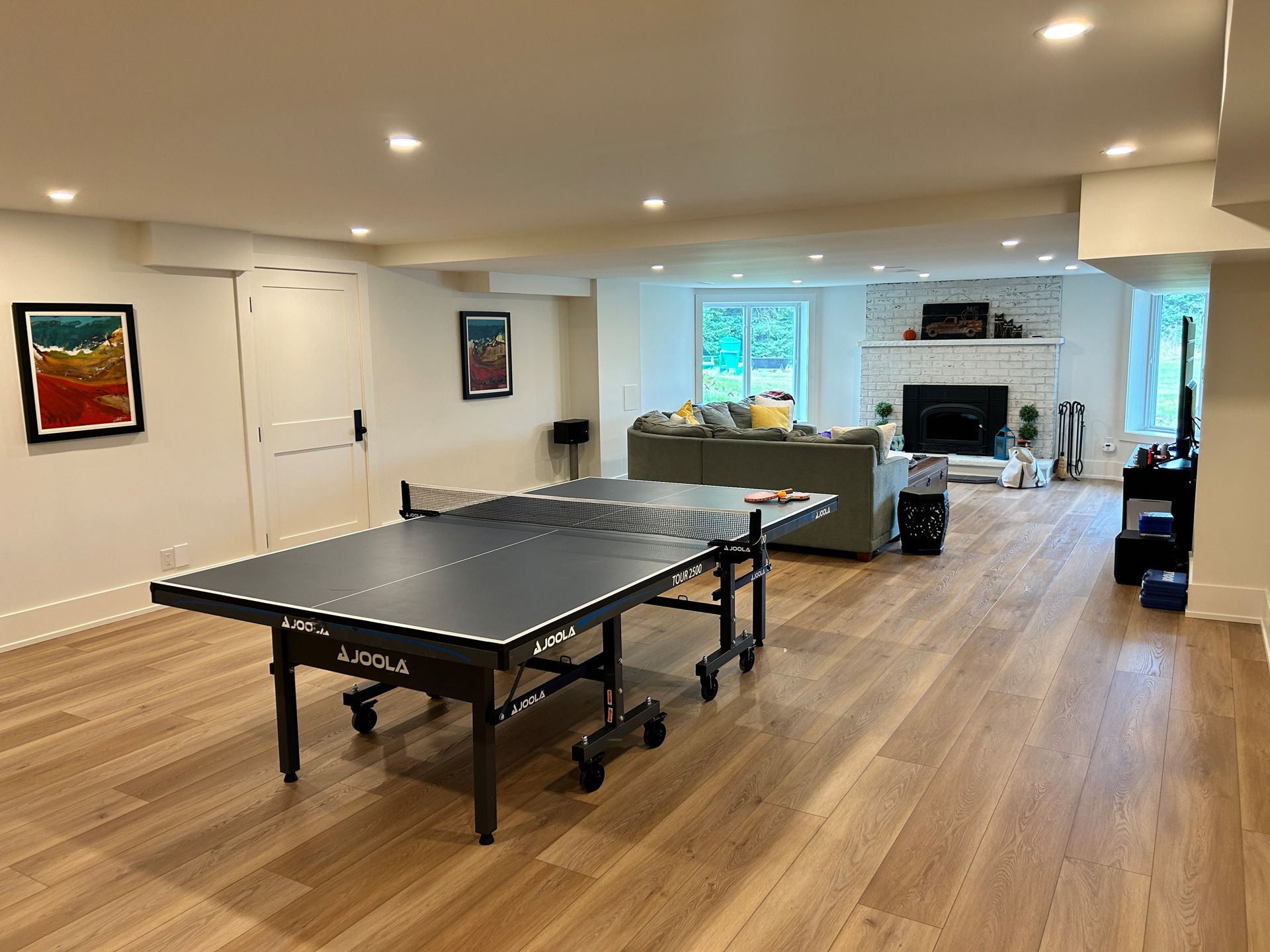 A modern finished basement with a ping pong table, seating area with fireplace, and hardwood floors.