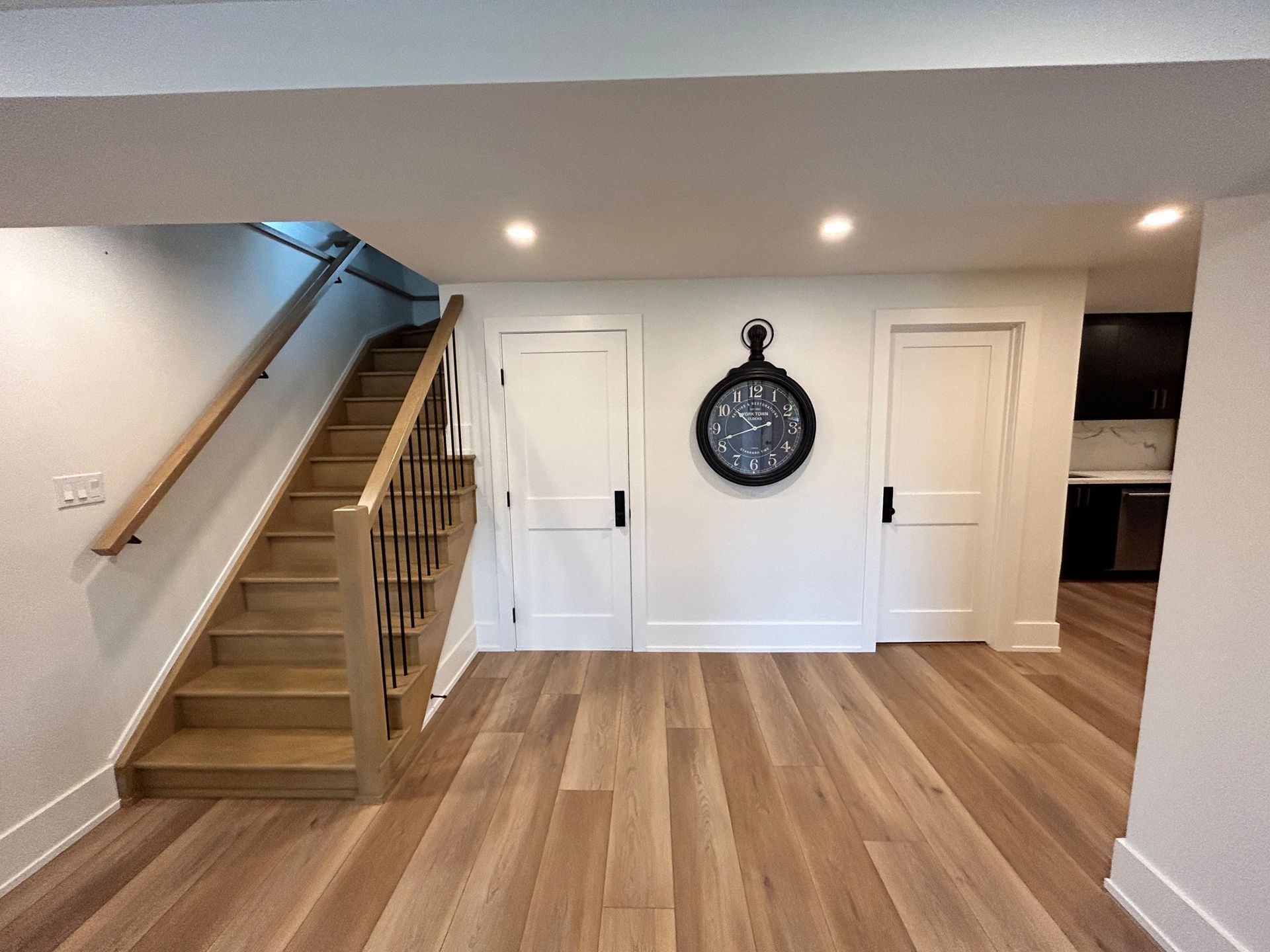 Wooden staircase and doors with a clock on the wall in a modern finished basement.