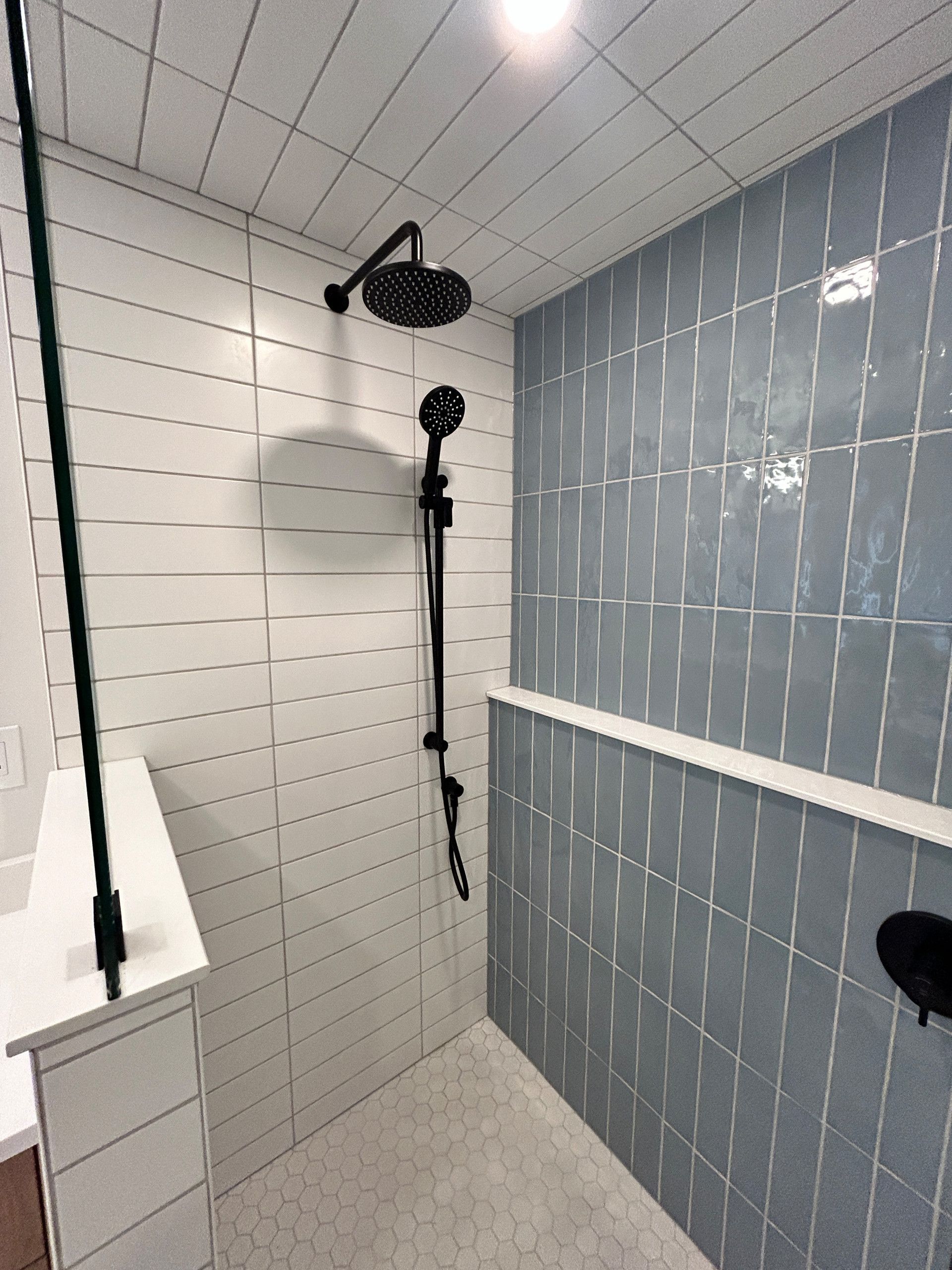 Shower with blue and white tiled walls, black shower fixtures, and a white shelf.