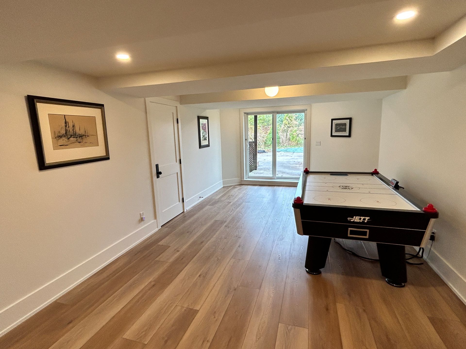 Basement room with air hockey table, wood floor, door to backyard, and framed artwork on the wall.