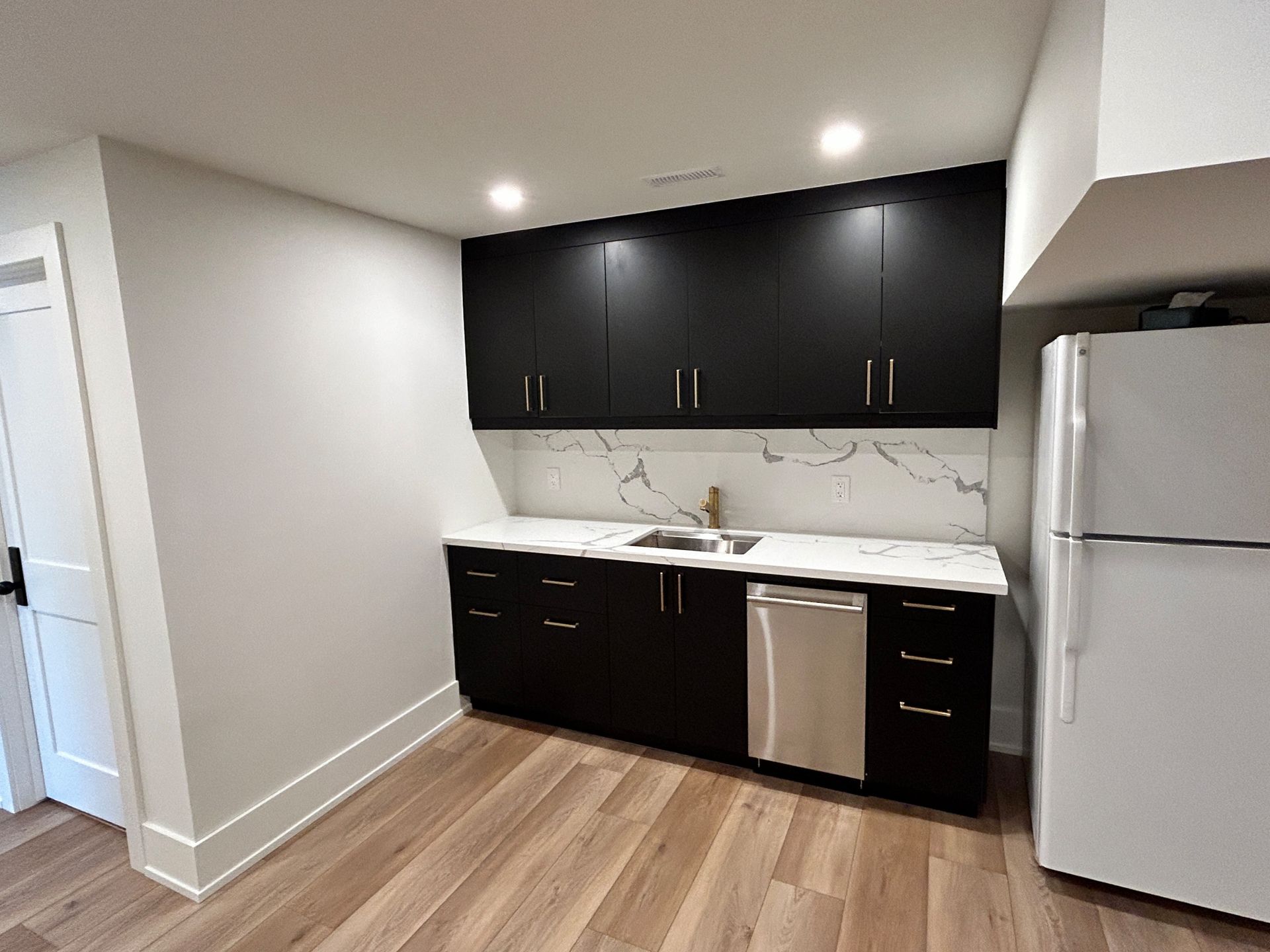 Black kitchen cabinets and a white refrigerator in a room with light wood flooring.