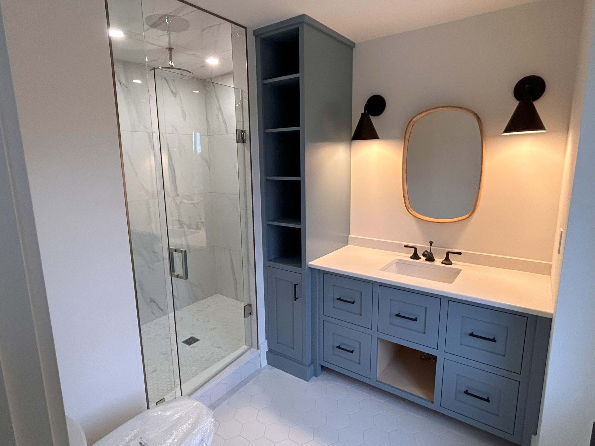 Blue bathroom with shower, vanity, mirror, and cabinet, illuminated by wall sconces.