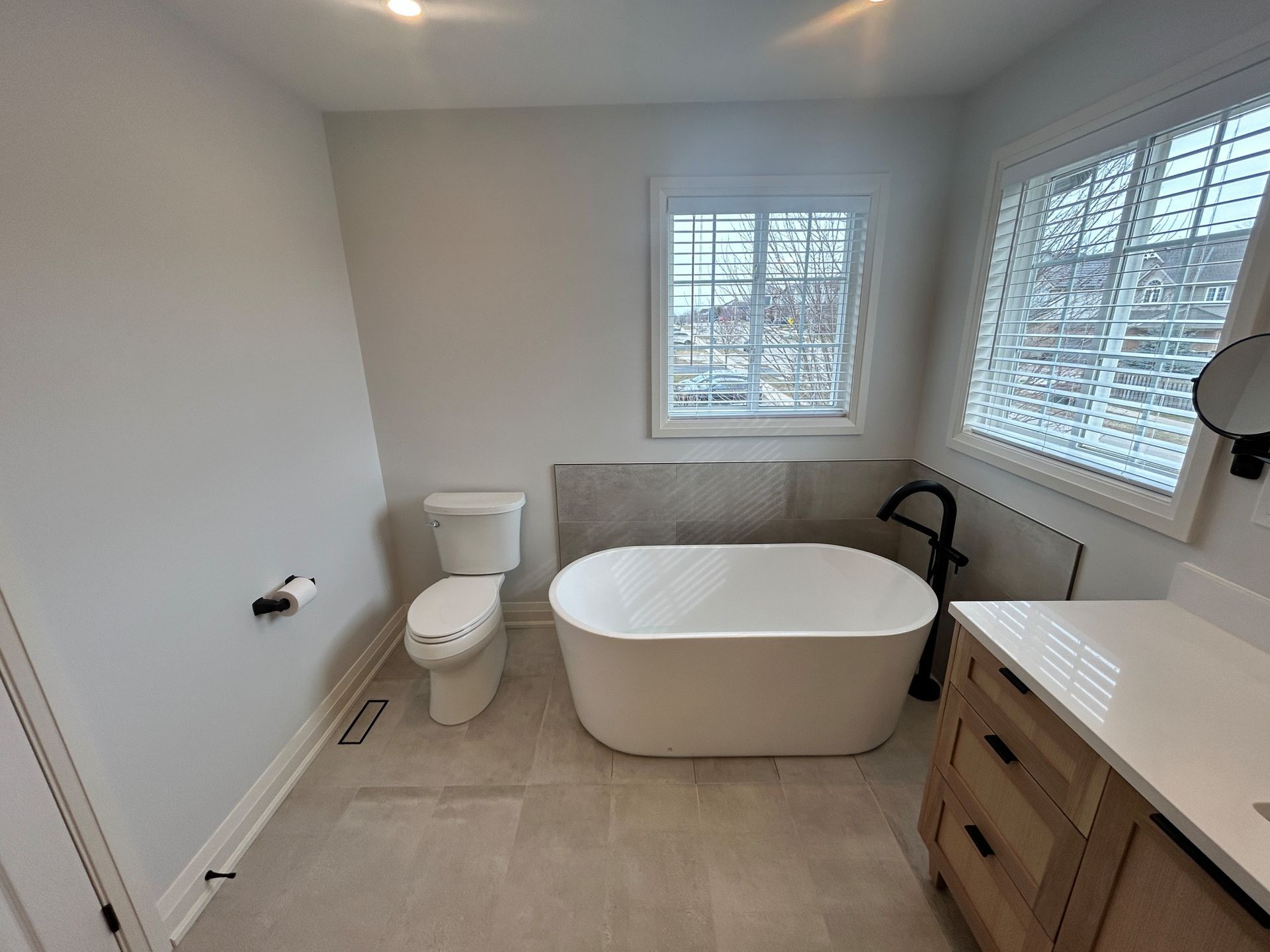 Bathroom with a freestanding tub, toilet, vanity, and a window with blinds.