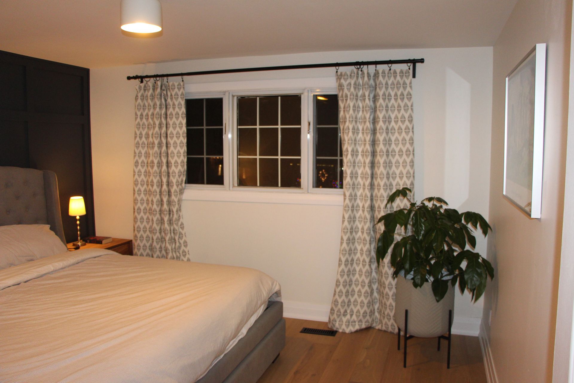 Bedroom with a bed, window with curtains, and a potted plant.