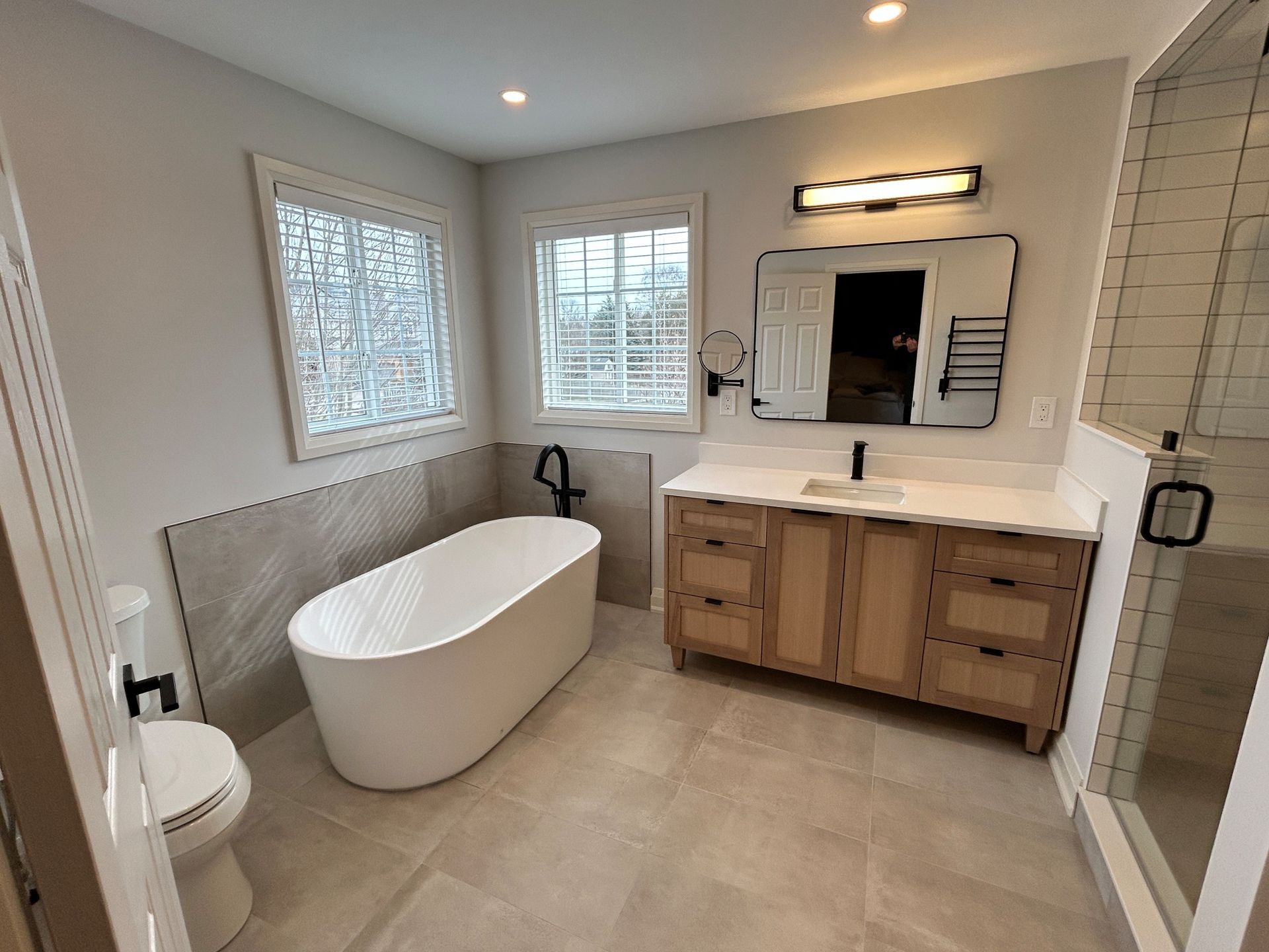 Modern bathroom with a white freestanding tub, wooden vanity, and a glass shower.
