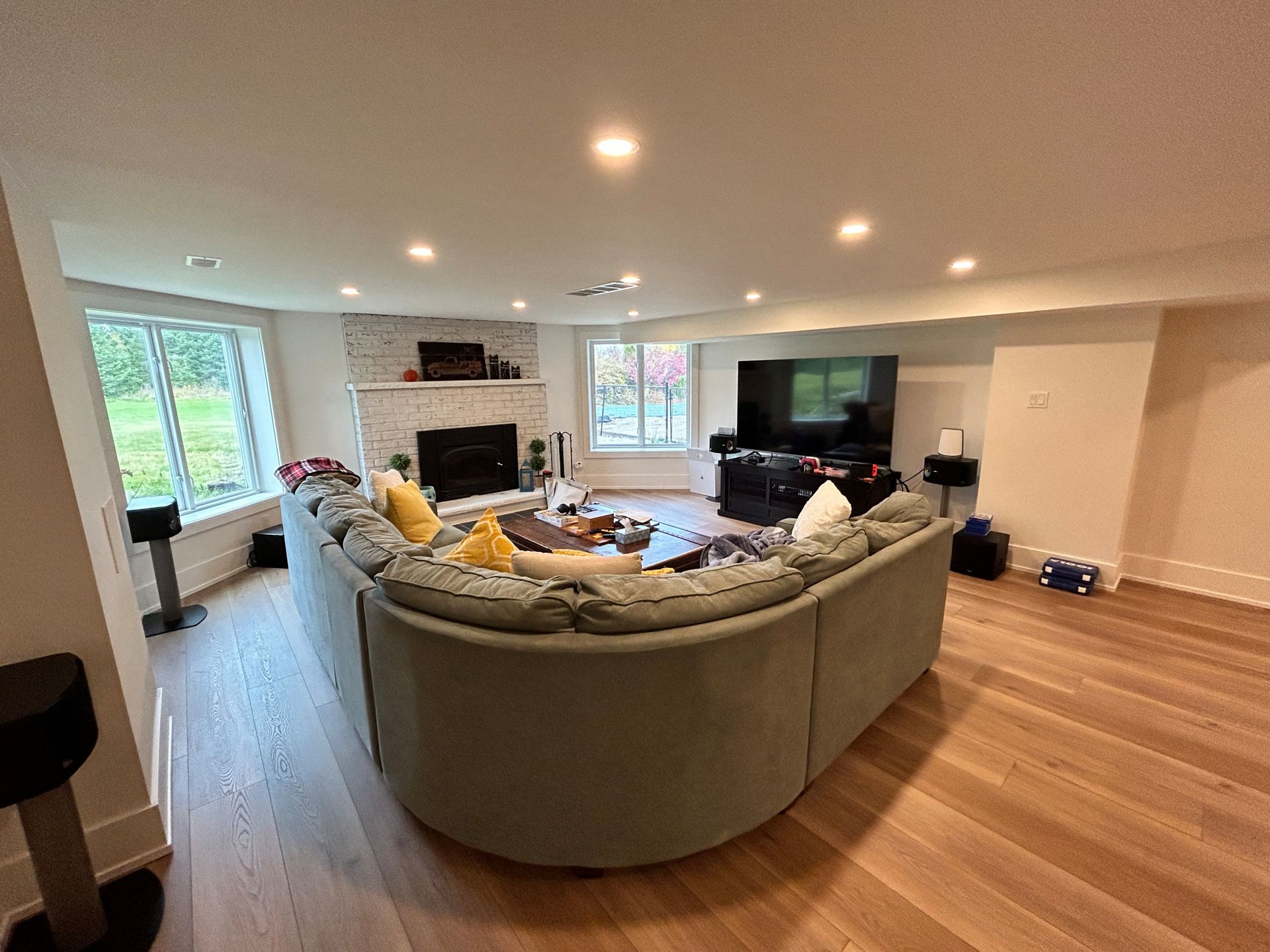 Spacious living room with a curved sofa, fireplace, TV, and large windows, hardwood floors.