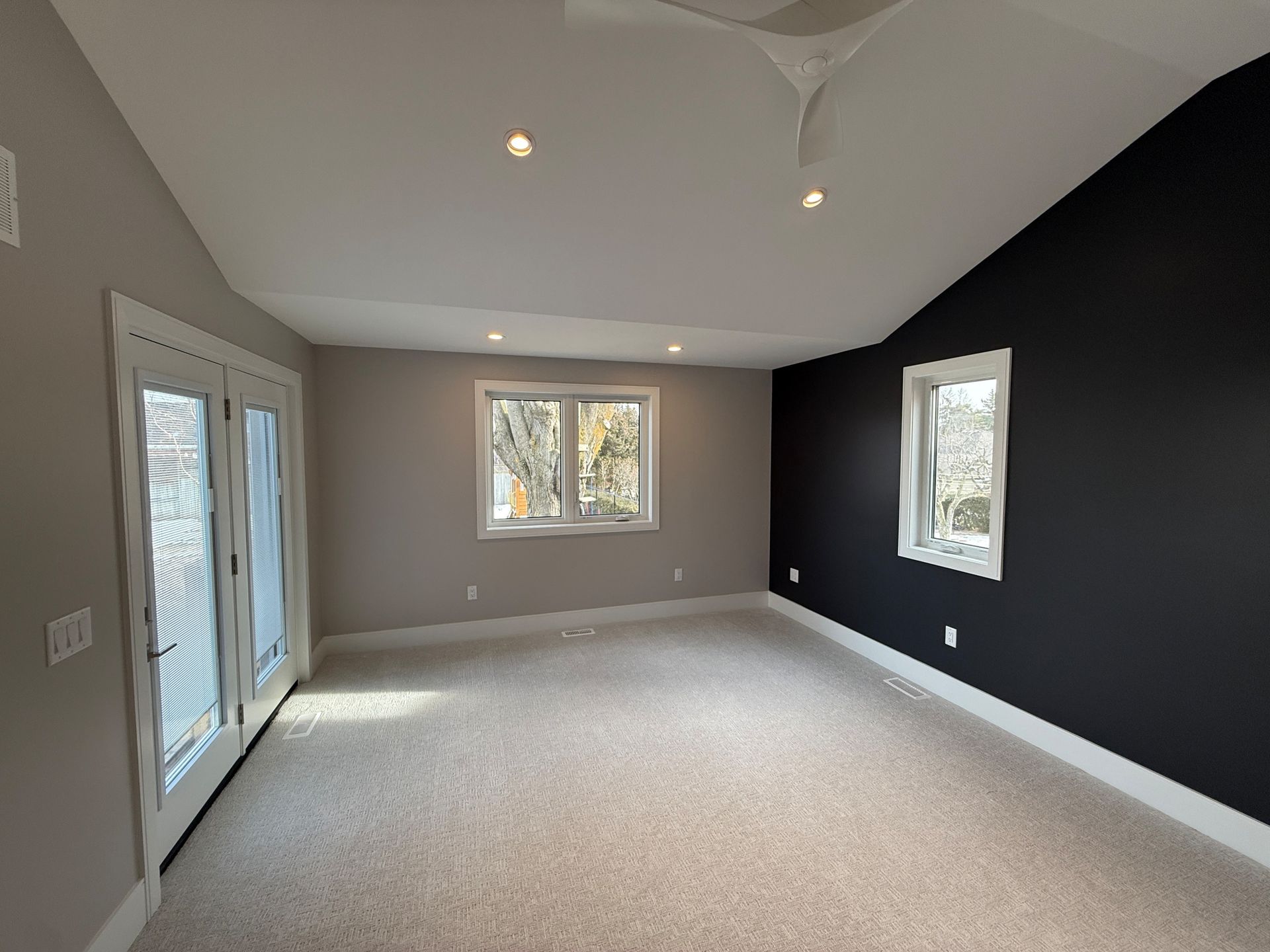 Empty bedroom with beige carpet, a dark gray accent wall, and white trim. French doors on the left.