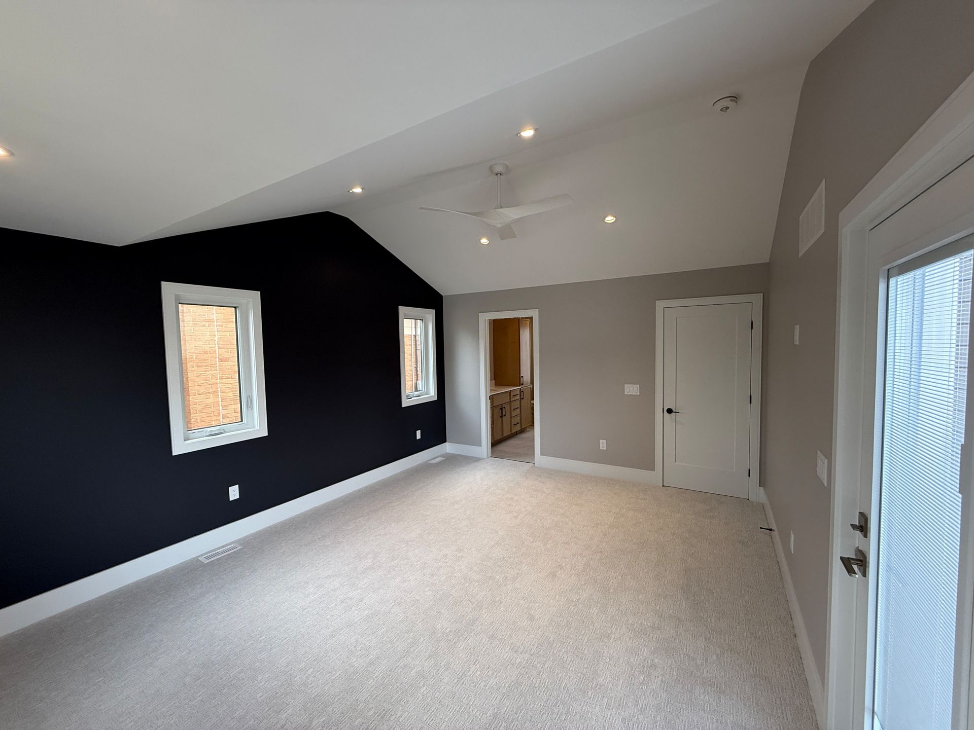 Empty bedroom with dark blue accent wall, white trim, gray walls, and light carpet.