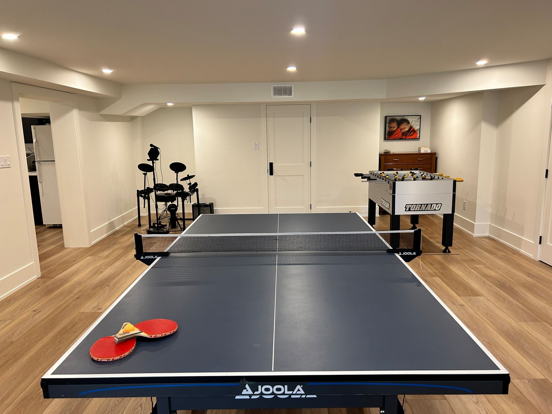 Ping pong table in a finished basement with drum set and foosball table.