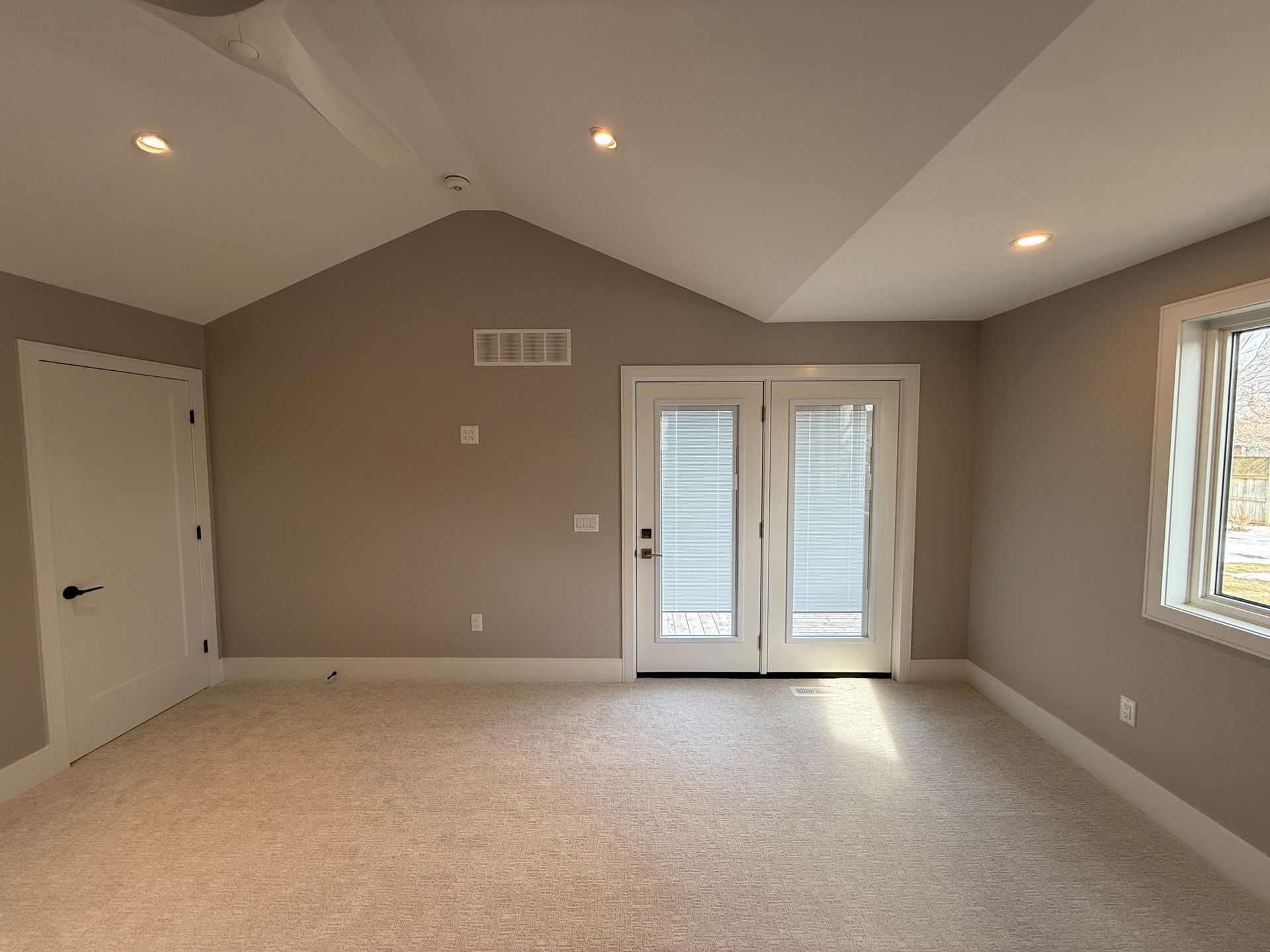 Empty room with tan walls and carpet, french doors, white trim, and recessed lighting.
