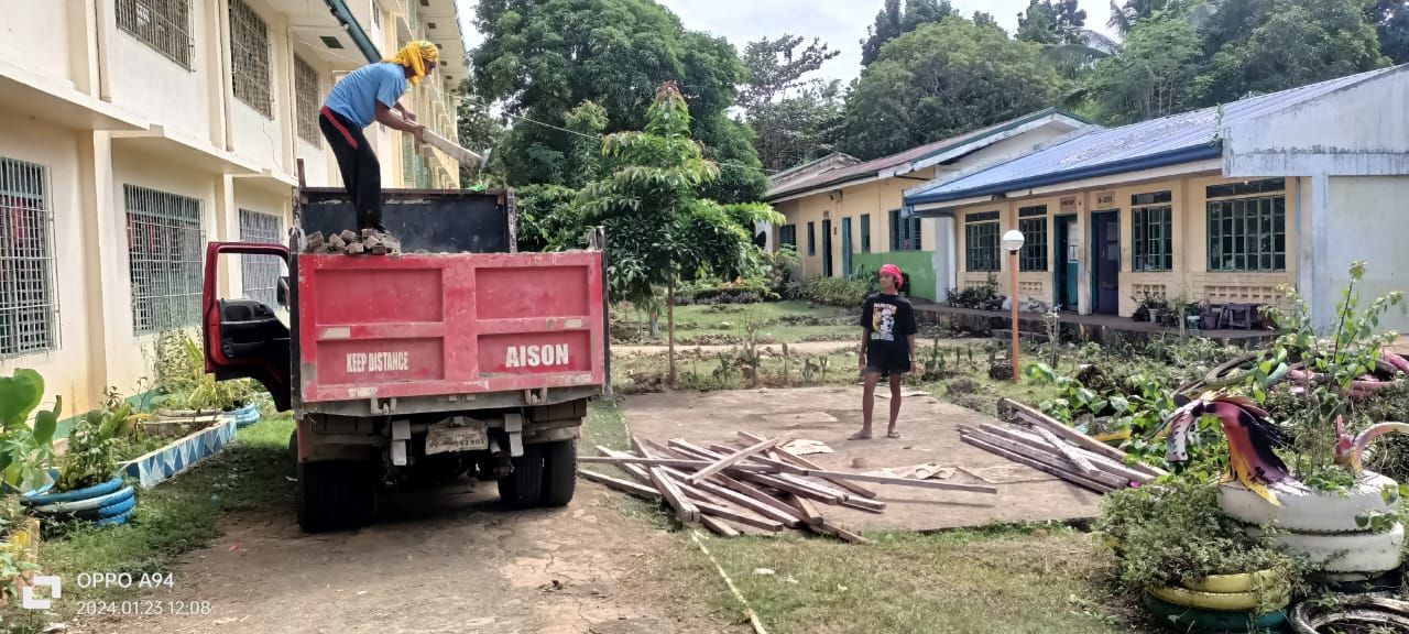 A man is standing on top of a red dump truck.