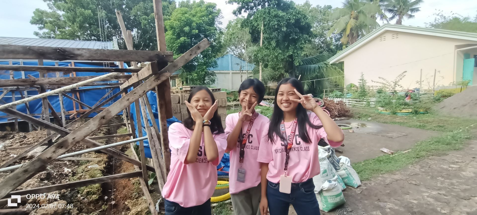 Three girls in pink shirts are posing for a picture in front of a building.