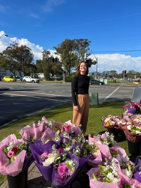 A woman is standing in front of a bunch of flowers.