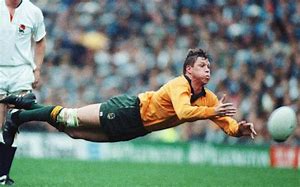 A man is diving to catch a rugby ball on a field.