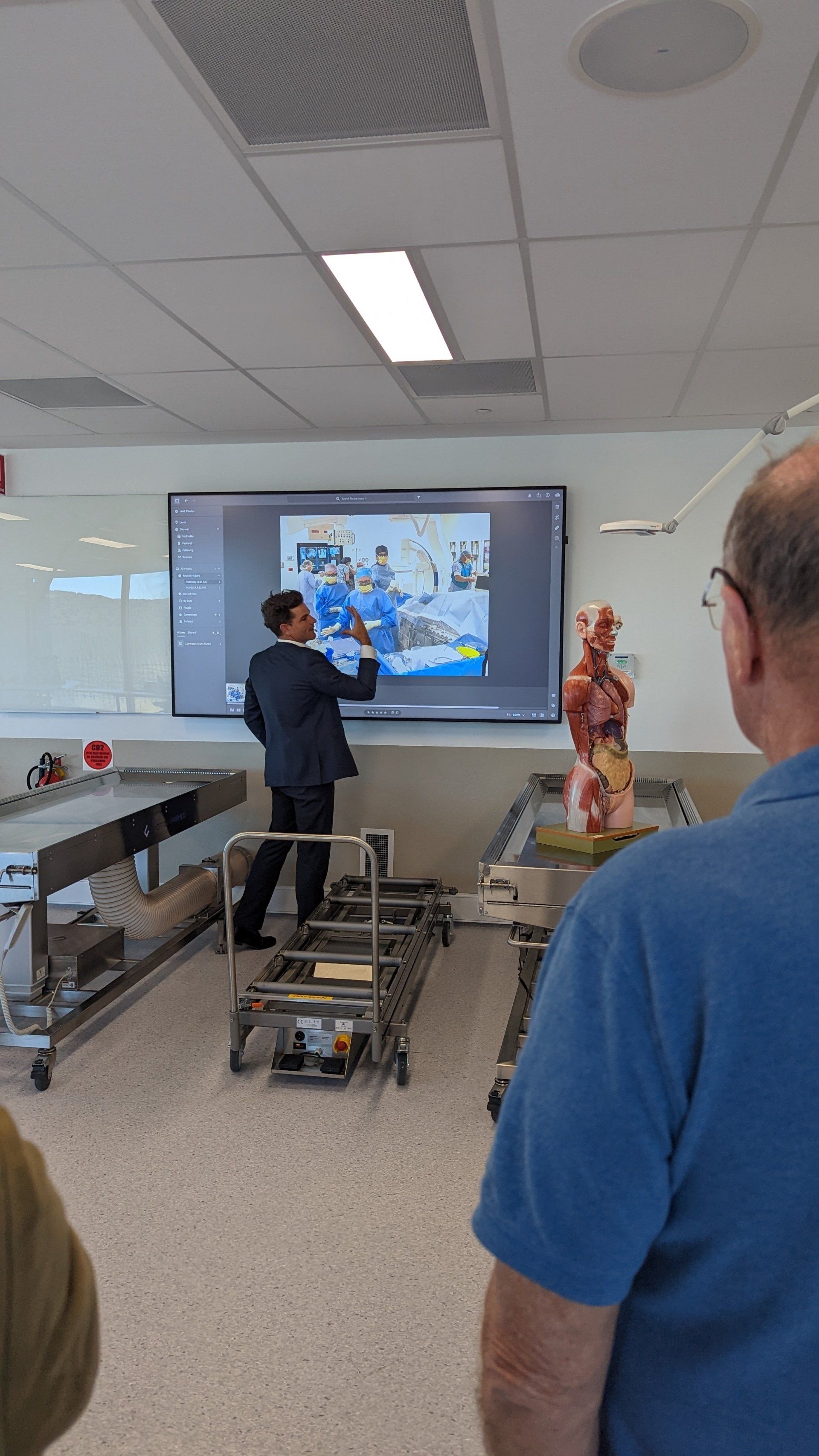 A man is giving a presentation in front of a large screen in a classroom.