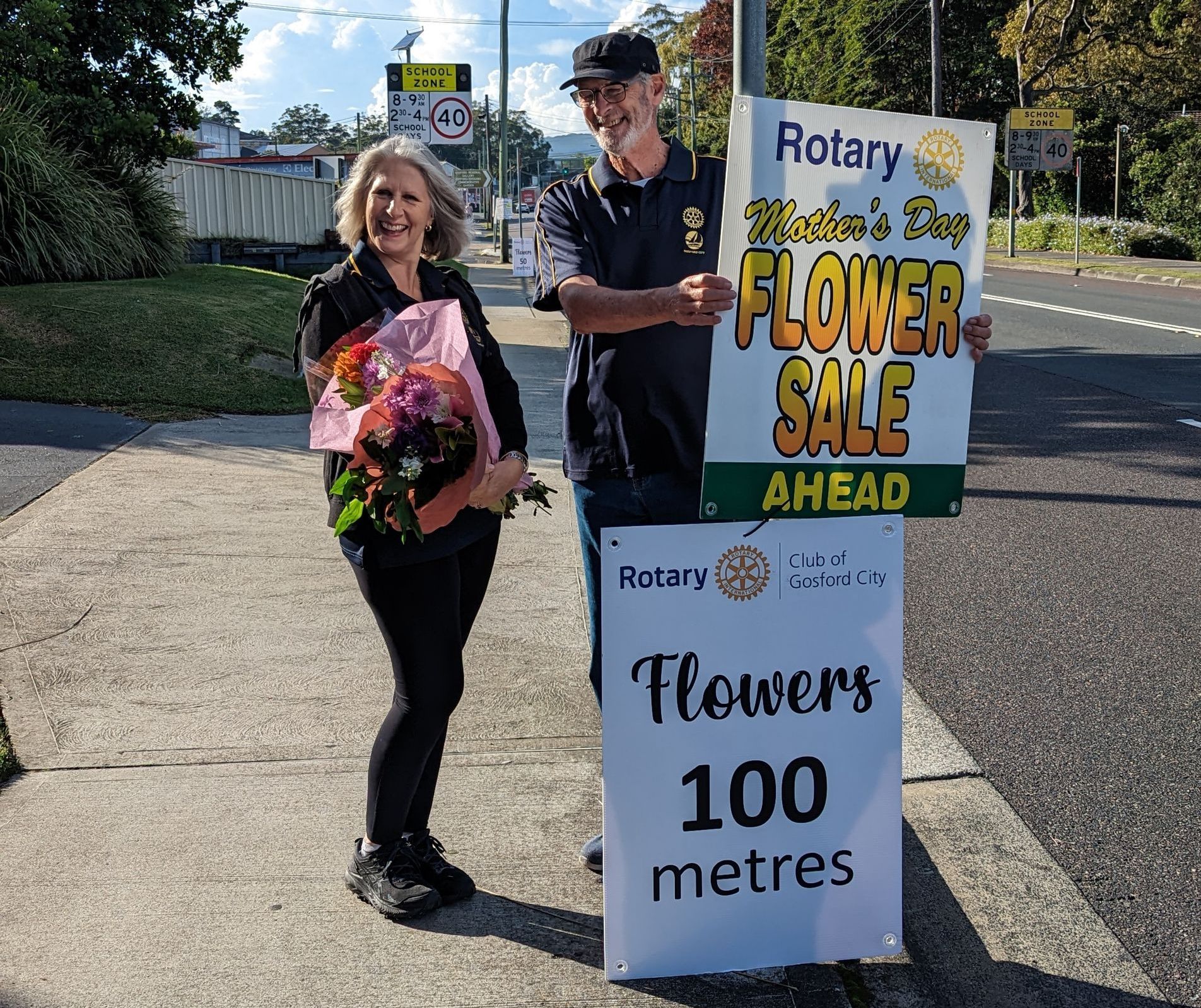 A man and woman holding a sign that says flowers 100 metres