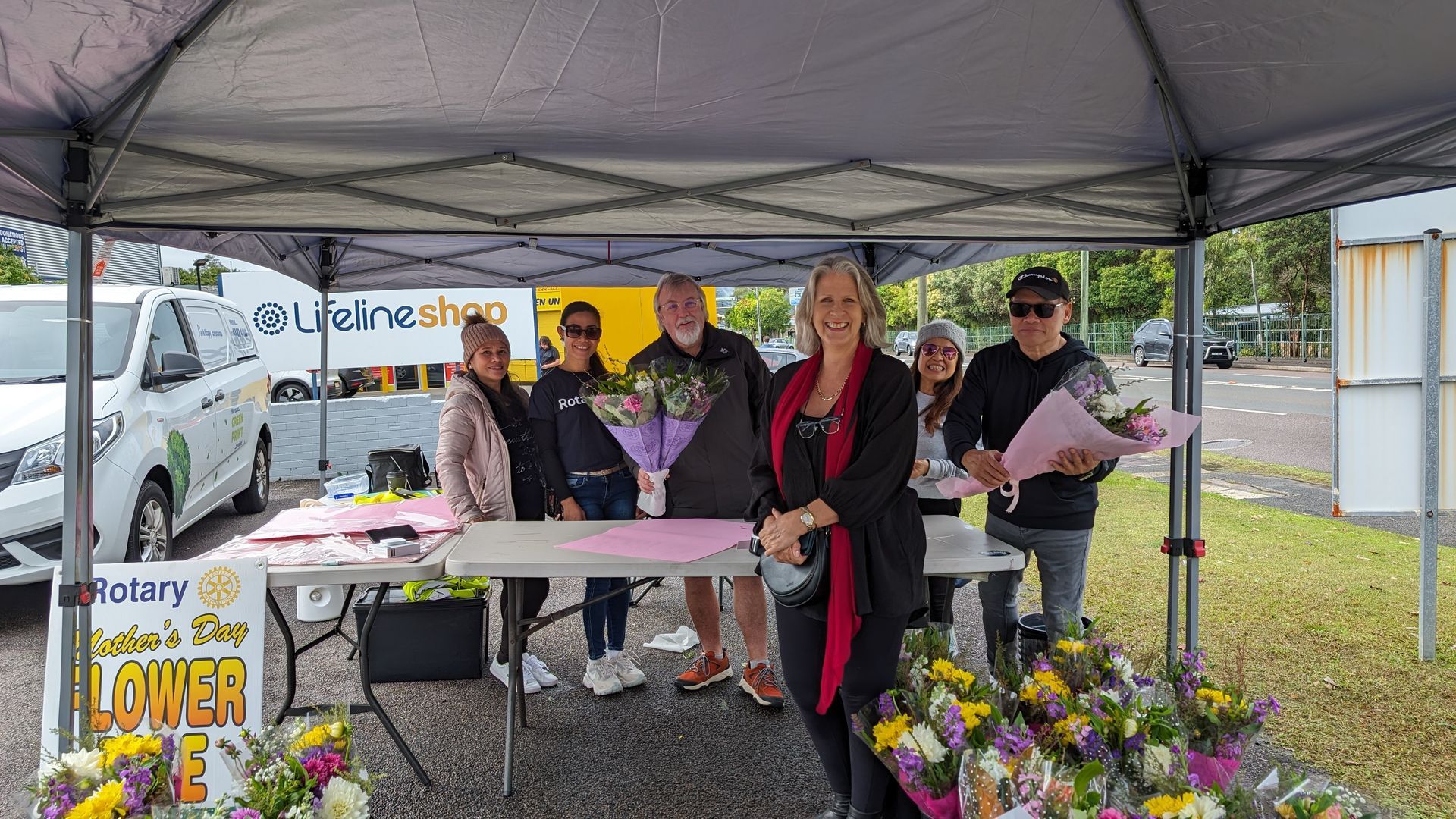 A group of people standing around a table with flowers under a tent.