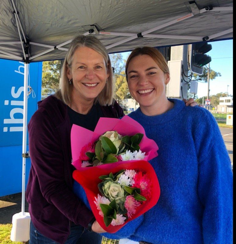 Two women holding bouquets of flowers in front of an ibis tent