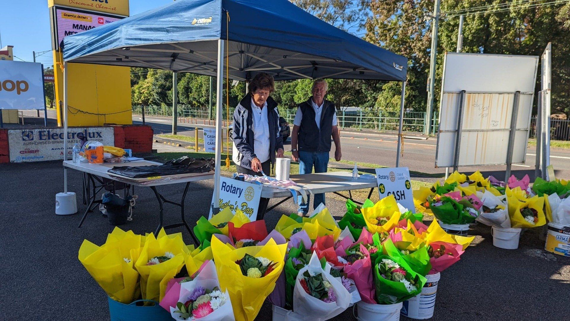Two men are standing in front of a tent filled with flowers.