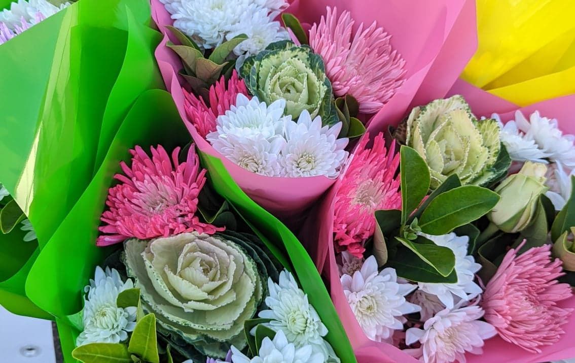 A bunch of flowers wrapped in pink and green paper are sitting on a table.