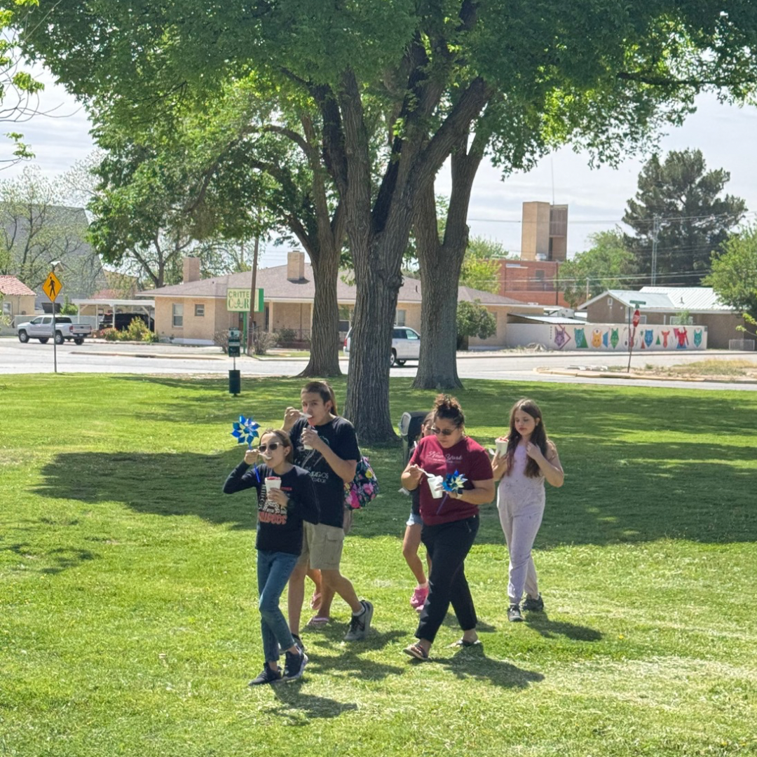 Children running across a sunny park lawn with trees and buildings in the background