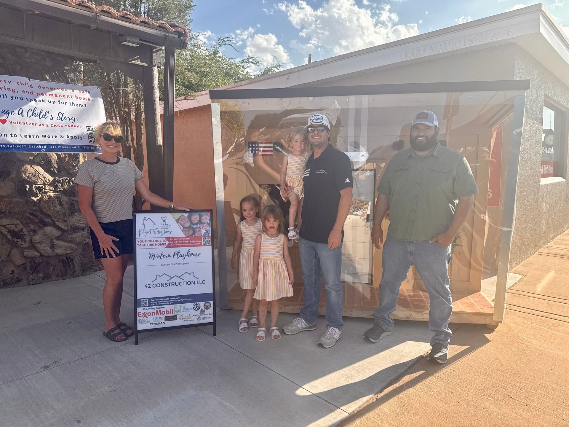 Four people and two children standing by a sign outside a tented outdoor event booth