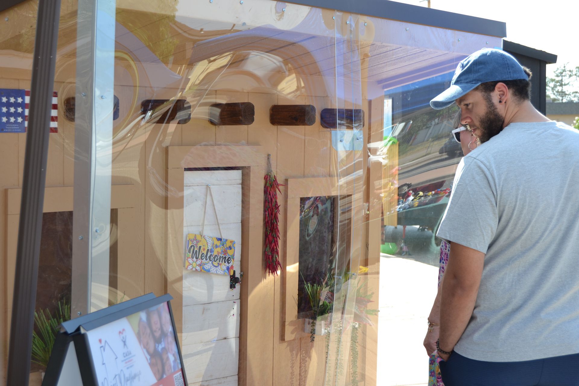 Man in blue cap looking at a window display with artwork and signs in a sunny storefront
