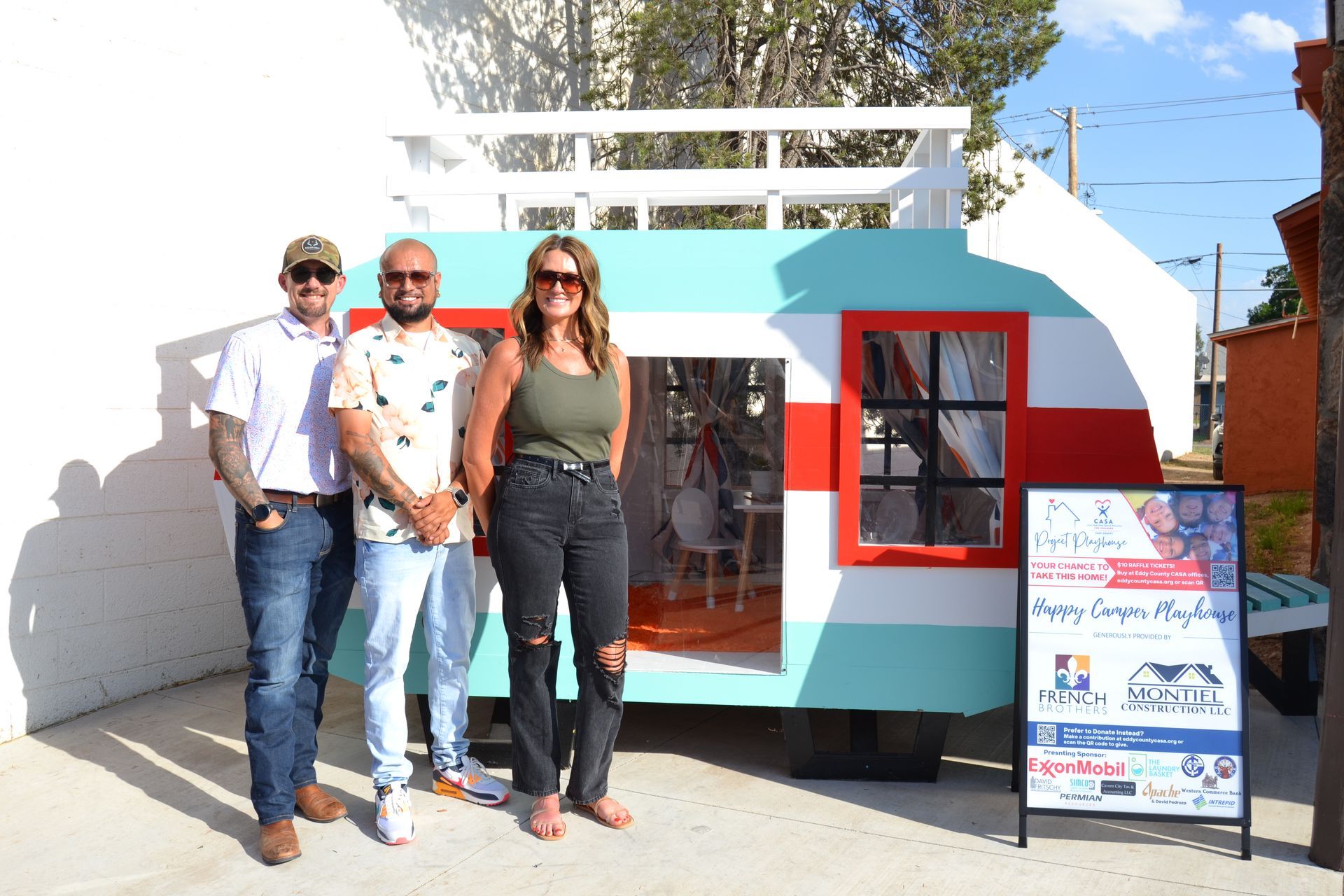Three people standing by a colorful kiosk with a signboard outside on a sunny day