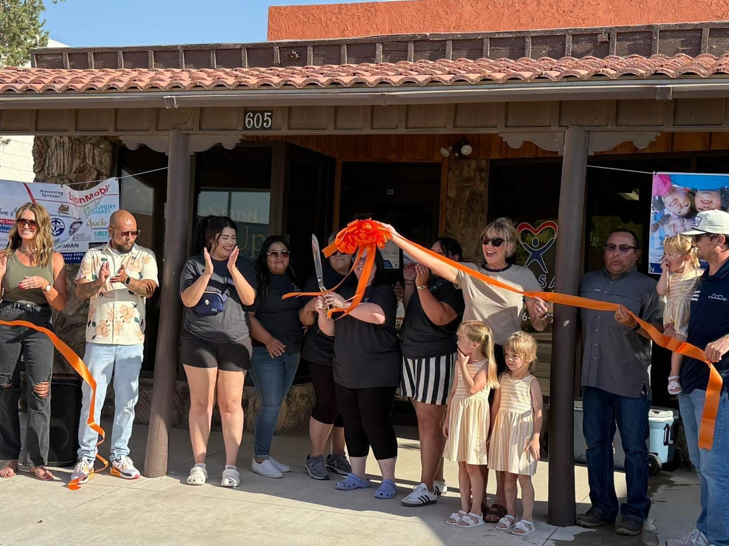 People gathered outside a building, holding an orange ribbon for a ribbon-cutting ceremony.