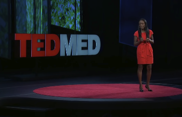 TEDMED stage with a speaker in a red dress under spotlight beside a large TEDMED sign