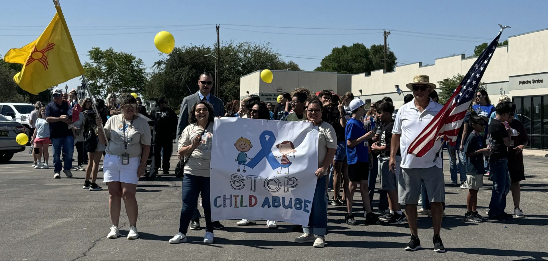 Protesters holding signs and balloons in a street march, including a banner reading “Stop Child Abuse”