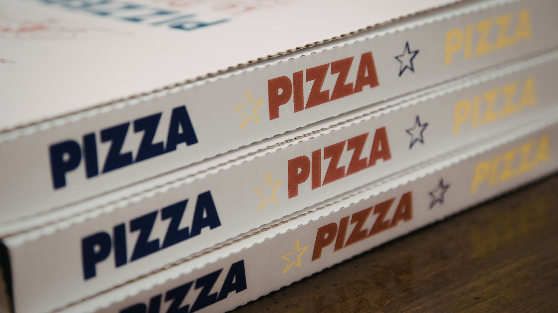Trois boîtes à pizza empilées avec l'inscription « PIZZA » en bleu et en rouille.