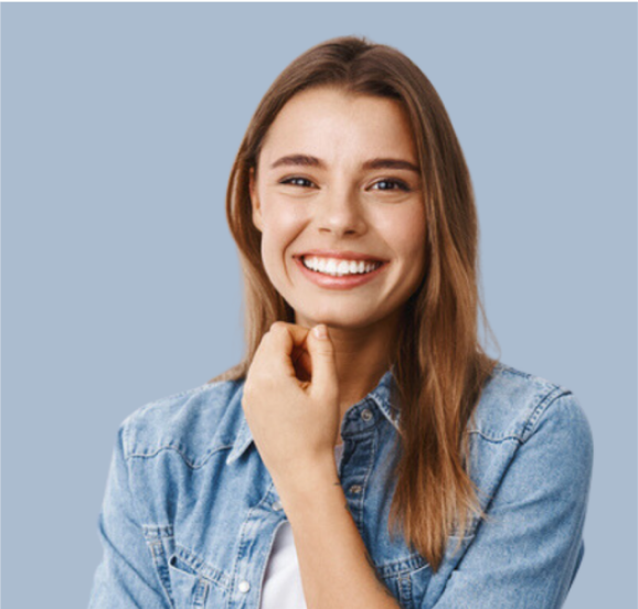 A woman in a denim shirt is smiling with her hand on her chin.