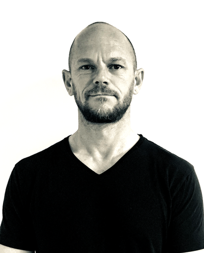 Portrait of a bald man with a beard wearing a black V-neck shirt against a white background