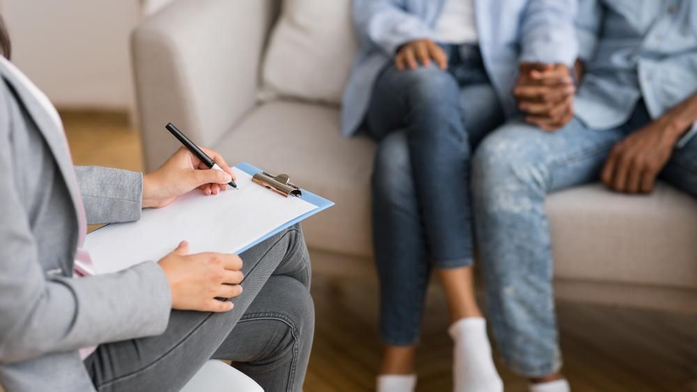 A Woman Is Writing On A Clipboard While A Man And Woman Sit On A Couch — Active Ables Community Services In Armidale, NSW