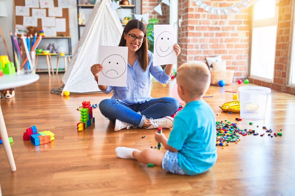 Woman and Toddler Playing on A Wooden Floor with Toy Blocks and Drawings in A Playroom — Active Ables Community Services In Brookwater, QLD