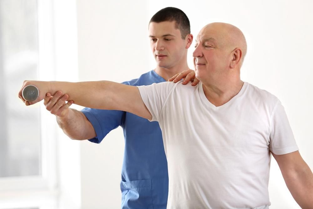 An Elderly Man Is Being Helped By A Nurse To Lift A Dumbbell — Active Ables Community Services In Tamworth, NSW