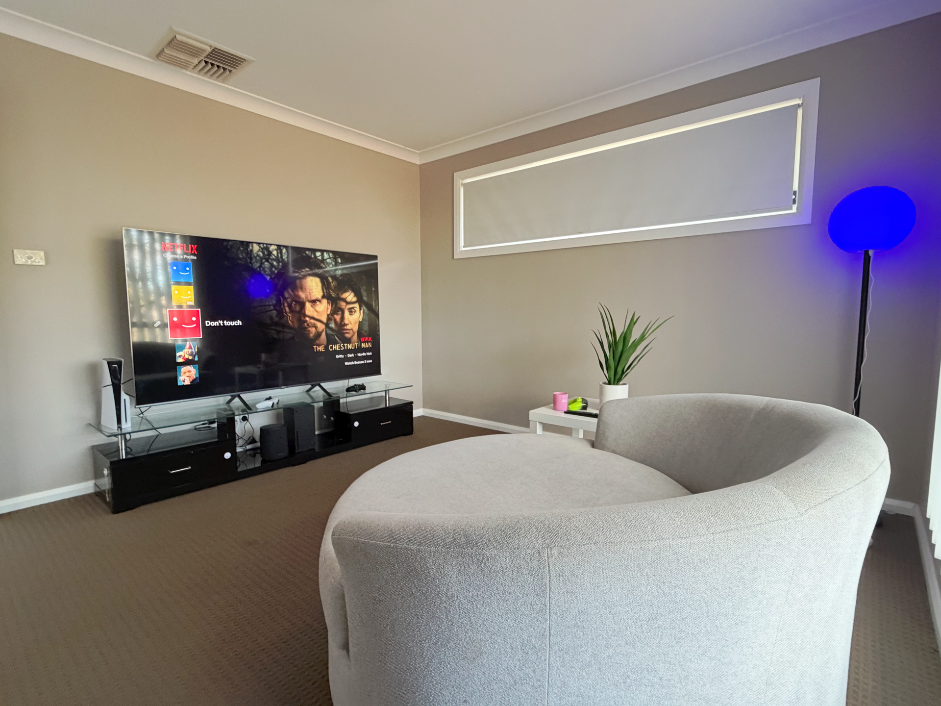 Modern living room with curved gray sofa, TV console, and blue floor lamp in the corner