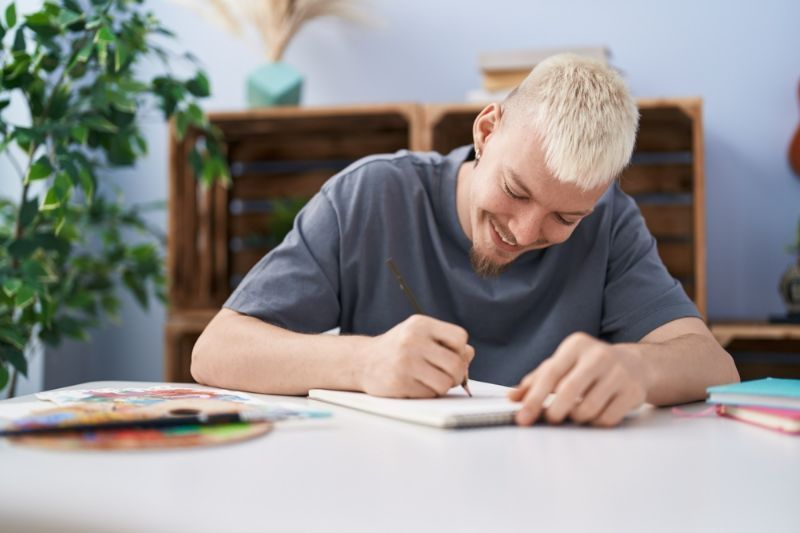 A Young Man Is Sitting at A Table Drawing with A Pencil — Active Ables Community Services In Inverell, NSW