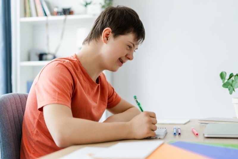 A Young Man Is Sitting at A Desk Writing on A Piece of Paper — Active Ables Community Services In Tamworth, NSW