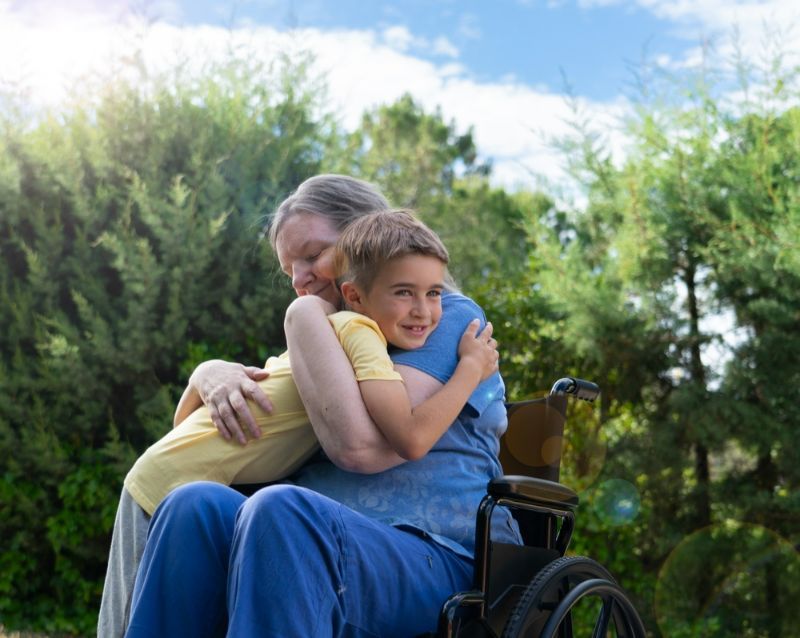 A Woman in A Wheelchair Is Hugging a Young Boy — Active Ables Community Services In Armidale, NSW