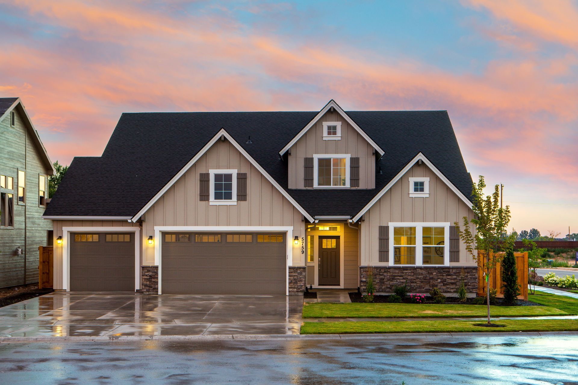 A modern two-story home at dusk with warm interior lighting, a large garage, and a manicured lawn under a blue sky.