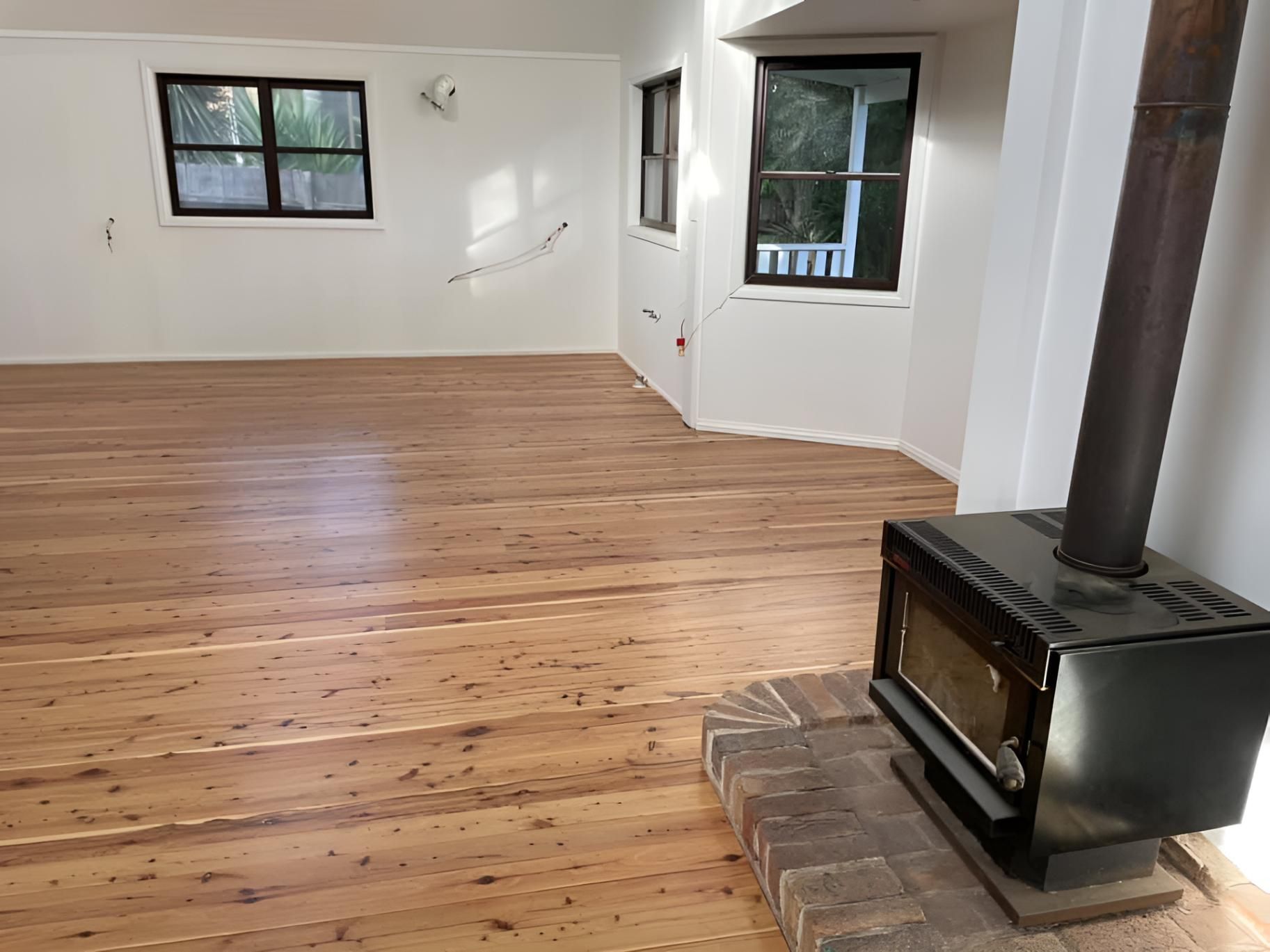 An Empty Room With Wooden Floors And A Wood Stove — Coolangatta Floor Sanding In Shoalhaven Heads, NSW